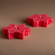 Two red snowflake-shaped candles on a plain brown background